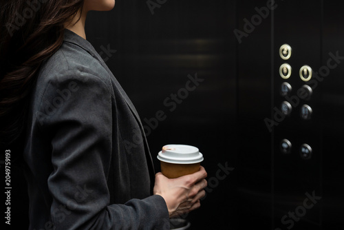 Close-up of a woman's hand holding a coffee cup inside elevator.