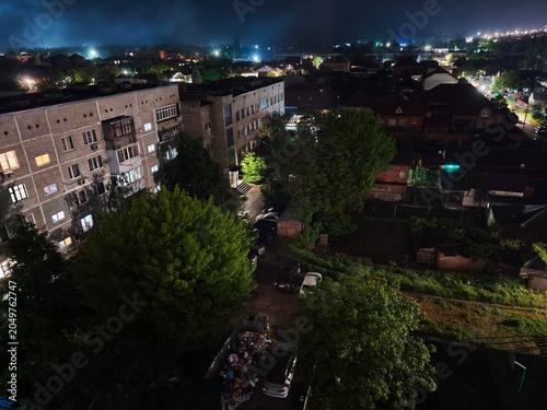 Night aerial view of courtyard with parked cars and dumpster in residential area