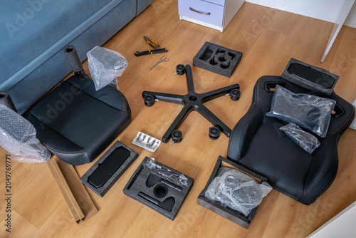 Quadro su tela Symmetrical top view of disassembled gaming chair parts, including seat, backrest, armrests, and base with casters, laid out on a laminate floor
