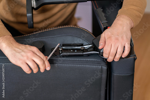 Canvastavla Detailed close up view of male hands tightening a screw with an wrench tool while assembling an ergonomic computer gaming chair at home