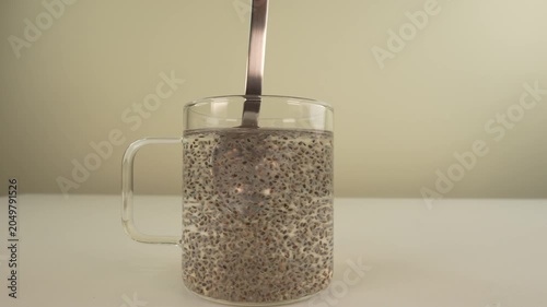 Stirring chia seeds with a spoon in glass cup of water.
