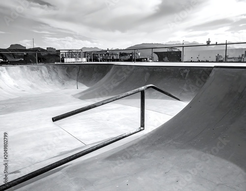 A black and white photograph of a skate park with a metal rail