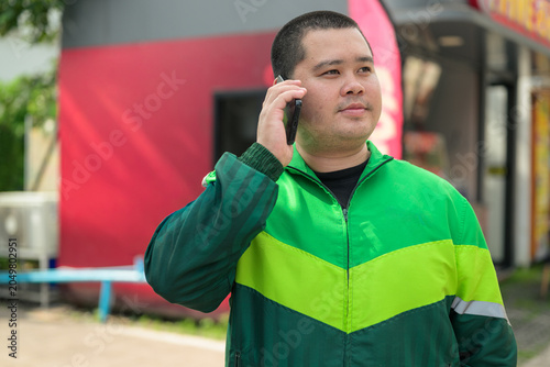 Plus size Thai delivery worker talking on smartphone outdoors near street landscape portrait
