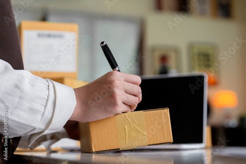 Entrepreneur hand writing customer details on cardboard parcel box using pen during online store shipping logistics and package delivery preparation process