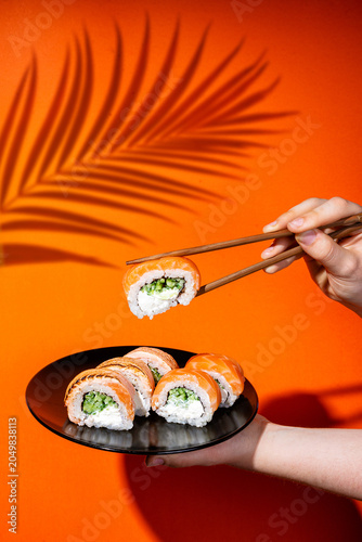 Hand dipping sushi roll in soy sauce on orange background