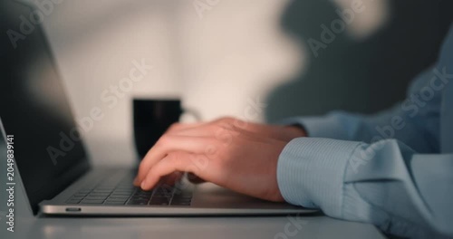 Business person typing fast on silver laptop keyboard during morning remote office work task.