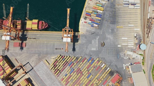 Stunning aerial top-down view of a bustling container port, showing gantry cranes actively unloading cargo from a large vessel docked at the quay, highlighting global trade and logistics