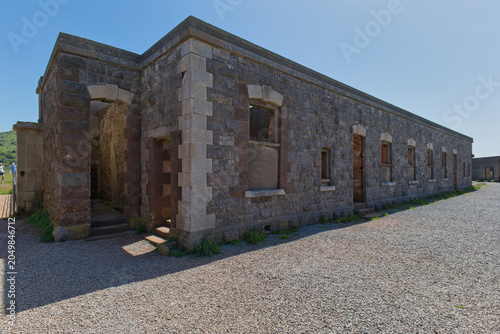 Obraz na plátne A long, historic stone building with numerous windows and doors stands on a grav
