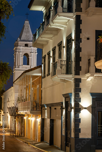 Historic San Jose church tower in San Felipe, casco viejo, Panama city, rising above charming colonial buildings with illuminated balconies and a cobblestone street at dusk - stock photo