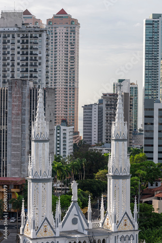 Ornate twin spires of El Carmen church prominently standing against a backdrop of modern residential and commercial skyscrapers in Panama city - stock photo