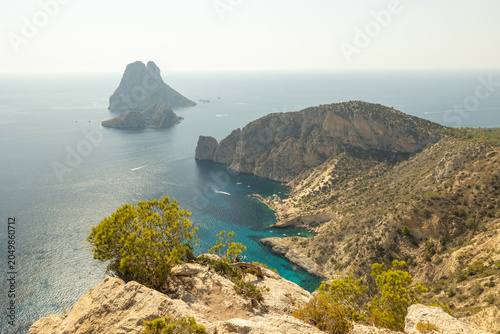 Bild auf Leinwand Panoramic view of the mysterious rocky island of Es Vedra rising from the Mediterranean Sea, seen from the rugged coast of Ibiza