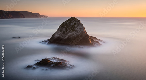 Sunset over a rugged coastline with majestic sea stacks and a misty long exposure ocean