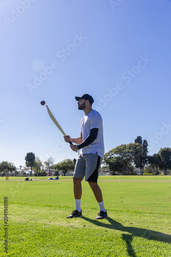 Cricket bat is being held in batting stance on grassy sports field near stumps, ball hovering