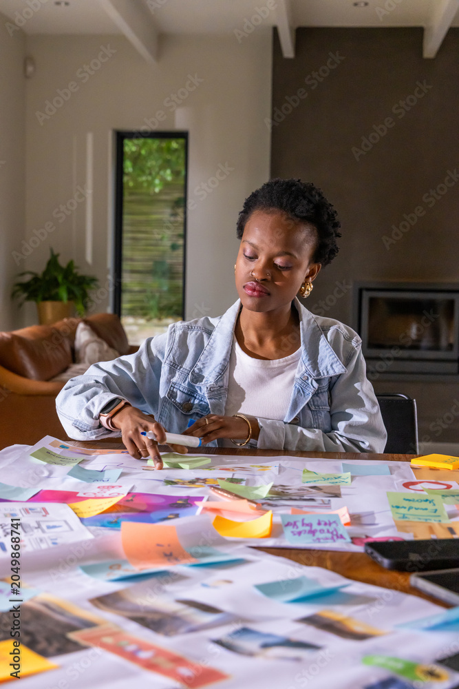 Obraz premium African American woman in denim jacket arranging sticky notes, pictures and papers at home