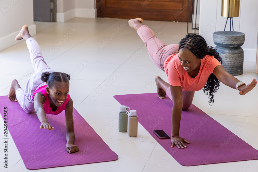 Fototapeta premium Mother and youth daughter exercising on purple mats at home, wearing coral and pink, bottles nearby