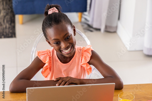 African American child in coral top smiling and using laptop at home with orange juice