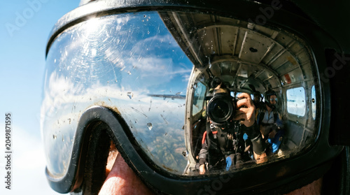 Skydiving helmet goggle reflection camera aircraft door adventurous jumper before freefall high above cloud with blue sky