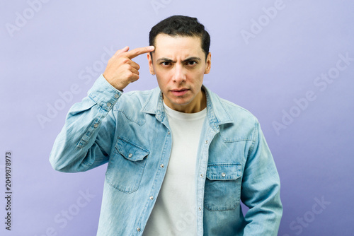 Billede på lærred Casual man pointing finger to temple on purple background, conveying a message t