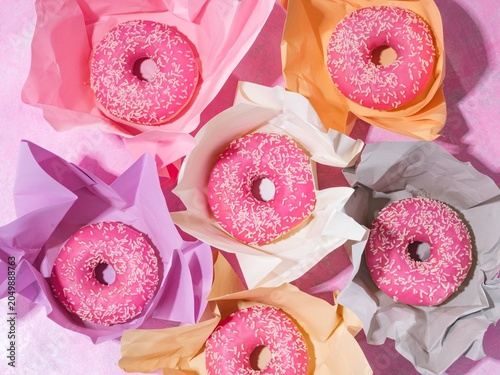 Bright pink donuts sprinkled with coconut flakes rest in cheerful pastel wrappers. These treats create a fun and inviting scene perfect for a celebration or a tasty snack