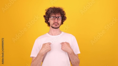 Surprised young person pointing at themselves with both hands in a bright yellow studio portrait, expressing shock, disbelief and a playful who, me? reaction.