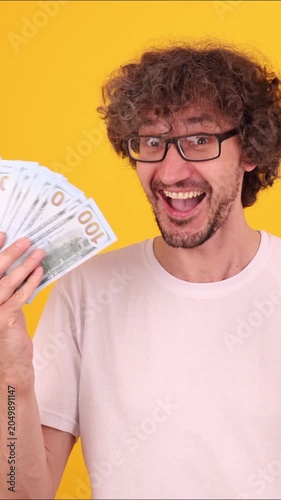 Person holding a fan of dollar banknotes and celebrating with a confident winner‑style mood against a bright yellow background.