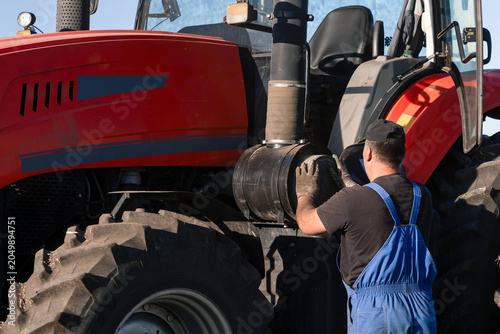 A tractor operator farmer takes out or installs an air filter in his tractor to clean, purge, or replace it. Maintenance of agricultural machinery in the field during sowing or harvesting.