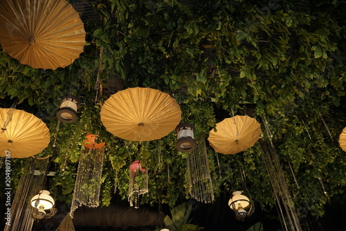 Decorative ceiling  featuring traditional golden paper umbrellas and vintage lanterns amidst hanging lush greenery foliage