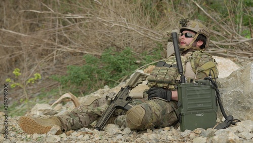 Fotografía A special forces soldier rests and rehydrates in a rugged environment, awaiting orders on his tactical radio during a demanding military mission
