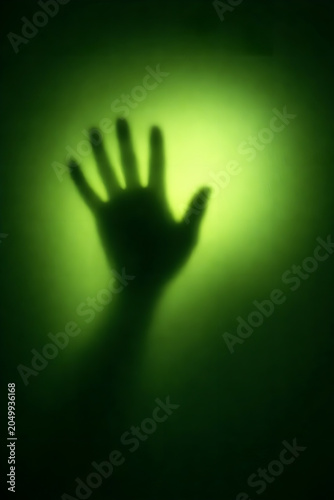 A mysterious silhouette of a hand pressed against a glowing green surface, illuminated from behind, symbolizing isolation, suspense, and modern art in a dark minimalist composition