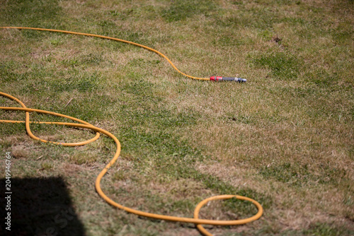 Detalhe de mangueira espalhada em cima da erva a ficar seca. Regar o jardim é importante.