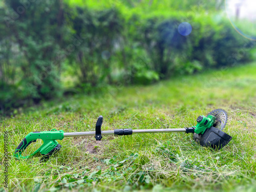 фотографія Cordless electric brush cutter with metal blade on freshly cut grass in backyard
