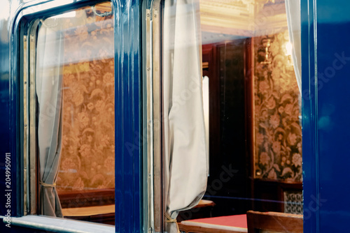 Konstfotografi Blue vintage train carriage window with ornate curtains and classic interior decor visible through glass