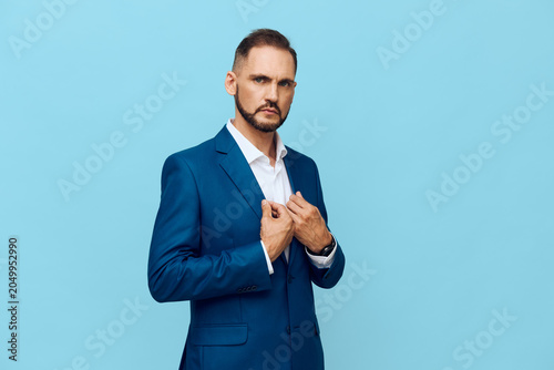 Принти на полотні A confident professional man in a blue suit stands against a solid blue background, projecting focus and determination while adjusting his jacket with poise in an isolated color setting