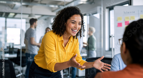 Smiling businesswoman leading a meeting and gesturing in modern office. Enthusiastic female manager explaining project to colleagues. Teamwork and collaboration concept