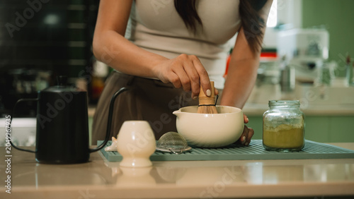Fotografi Close Up of Hands Making Matcha Tea with Bamboo Whisk in Ceramic Bowl on Kitchen