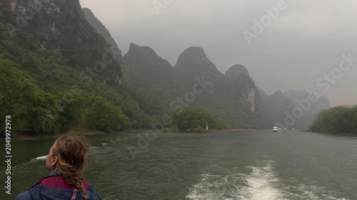 Slow motion back view of female tourist on cruise boat looking at foggy karst mountains along Li river in Guilin China