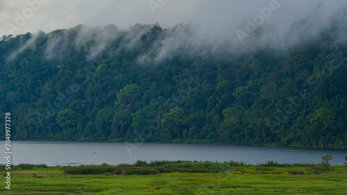 Konstfotografi Scenic view of Lake Buyan in Bali with dramatic low clouds and mist rolling over a lush green tropical rainforest mountain landscape