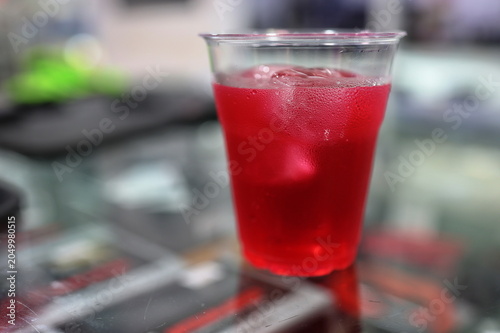 Fotografie A dark red drink with ice is served in a clear plastic cup with condensation around the rim
