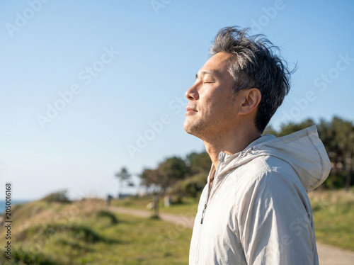 Asian Man Breathing Fresh Air in Green Field on Sunny Day