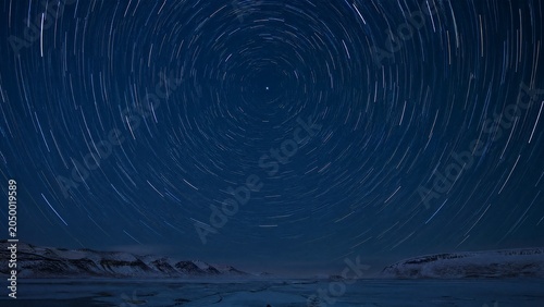 Arctic night sky with star trails circling a bright Polaris star in dark blue tones.