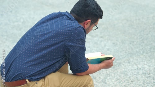 A man reads a book while sitting in a public plaza in Chicago. The scene shows concentration and quiet moments in a busy urban environment.