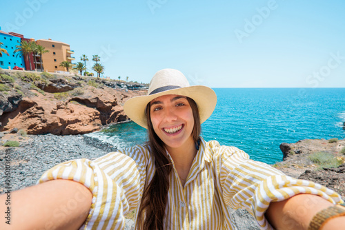 Photos Young woman wearing a hat and striped shirt smiling, holding a phone for a selfi