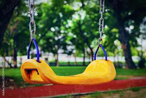 Photos Yellow plastic children's swing seat with chains hanging in a shady public park