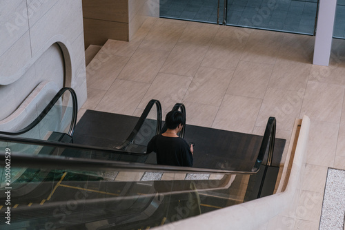 Billede på lærred Man in black shirt descending an escalator in a modern shopping mall, absorbed i