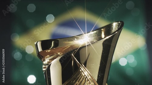 Gold trophy cup shining with light glint against blurred brazil flag. 4K Video