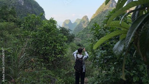 Slow motion back view of male tourist with backpack taking photo of scenic karst mountains on hiking trail in Yangshuo China