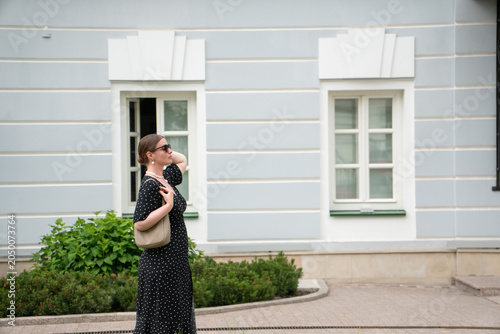 Obraz na płótnie Woman in black polka dot dress, minimalist historic facade and landscaped surroundings creating elegant urban lifestyle scene