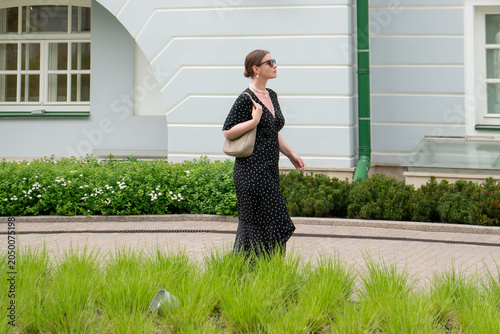 Quadro su tela Woman in black polka dot dress walks through courtyard of Yeltsin Center Moscow branch, with manicured greenery and historic architecture