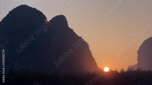 Time lapse of beautiful golden sunset with sun setting behind dramatic karst mountain silhouettes in China