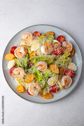 Caesar salad with tiger prawns, cherry tomatoes, croutons, parmesan cheese, quail eggs and romaine lettuce. Traditional American dish. Close-up, selective focus.
